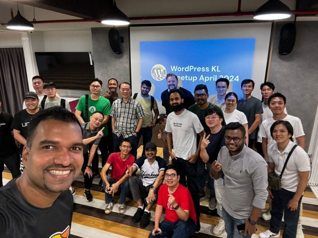 A group of people poses for a photo in front of a screen displaying "WordPress KL Meetup April 2024" in a conference room.