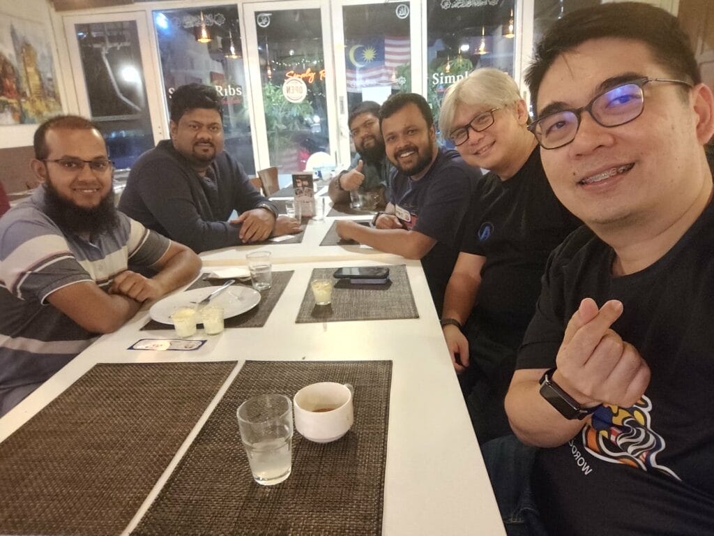 Six men sitting around a restaurant table with drinks and dessert plates, smiling at the camera.