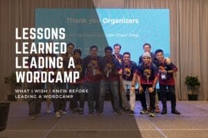 A group of people in matching t-shirts stands on a stage in front of a screen displaying "Thank you Organizers" and "Lessons Learned Leading a WordCamp.
