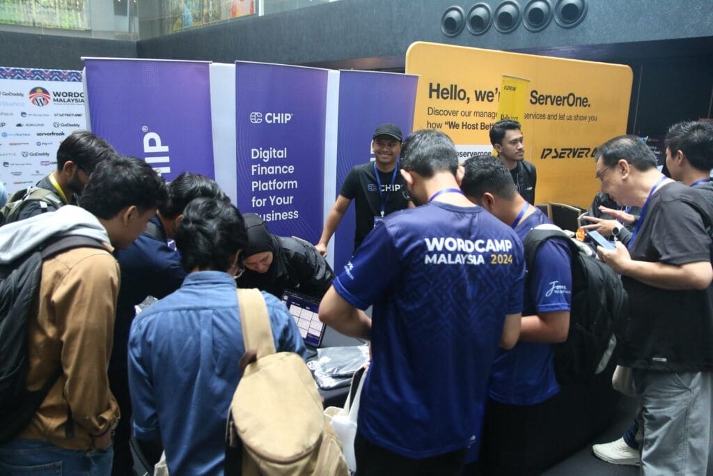 A group of people gather around a booth with CHIP and ServerONE banners at a WordCamp Malaysia 2024 event.