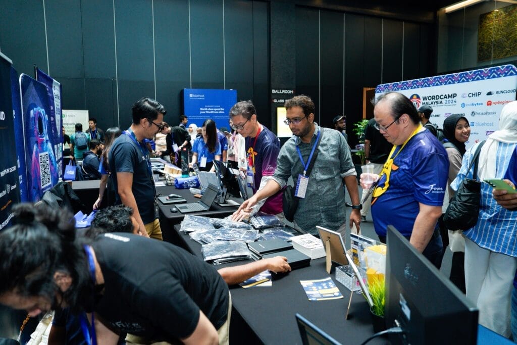 People browse and interact at exhibition booths during a technology conference in a large indoor venue.