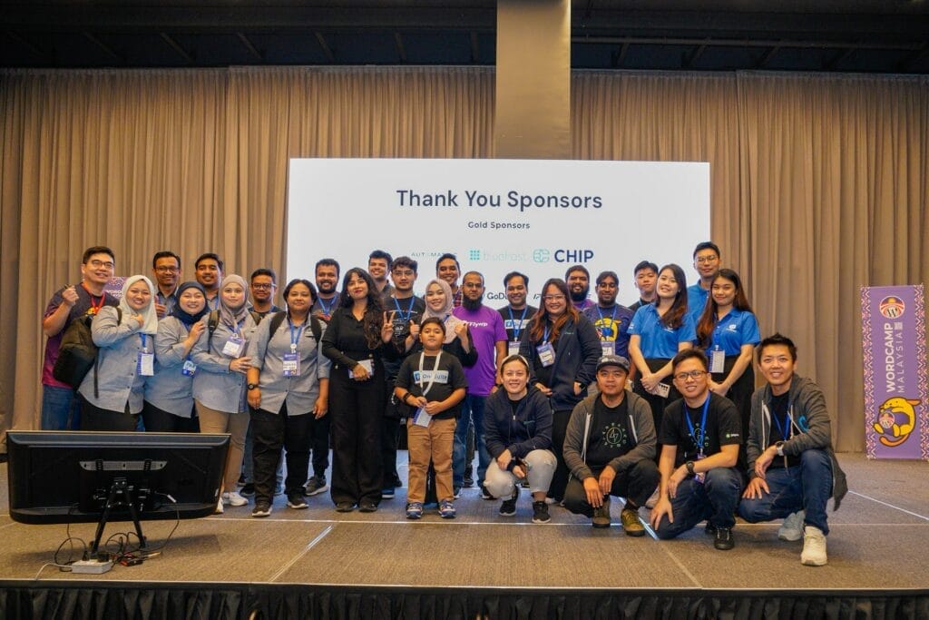 A group of people poses on stage in front of a "Thank You Sponsors" sign at an event, with sponsor logos and a curtain backdrop visible.